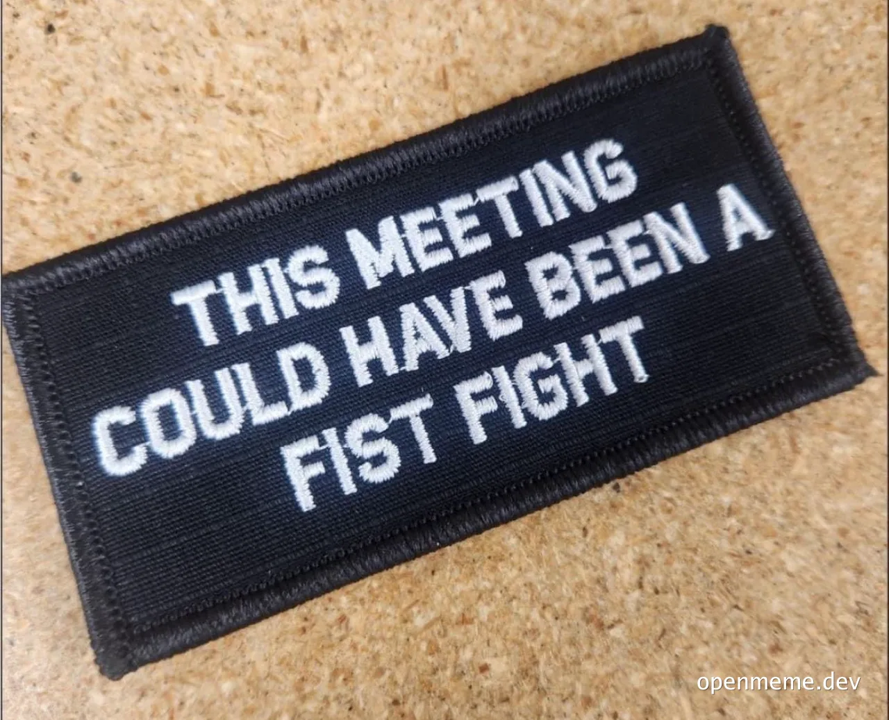 a black embroidered patch with white text that reads 'THIS MEETING COULD HAVE BEEN A FIST FIGHT'