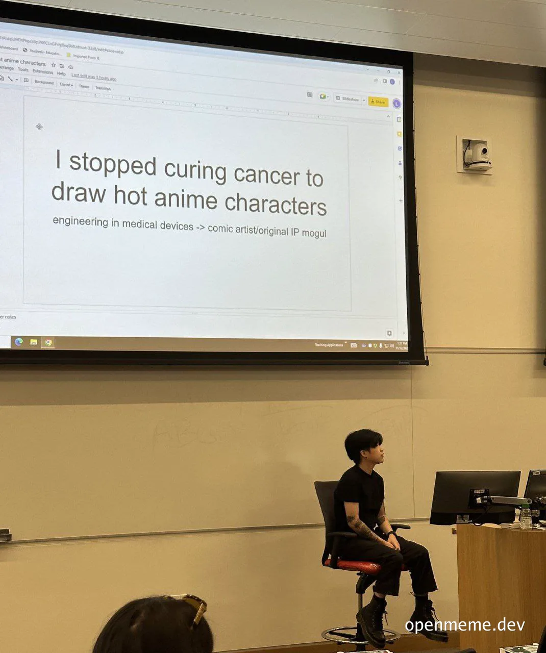 a woman sits in front of a projector screen with a humorous message about quitting medical device engineering to draw anime characters