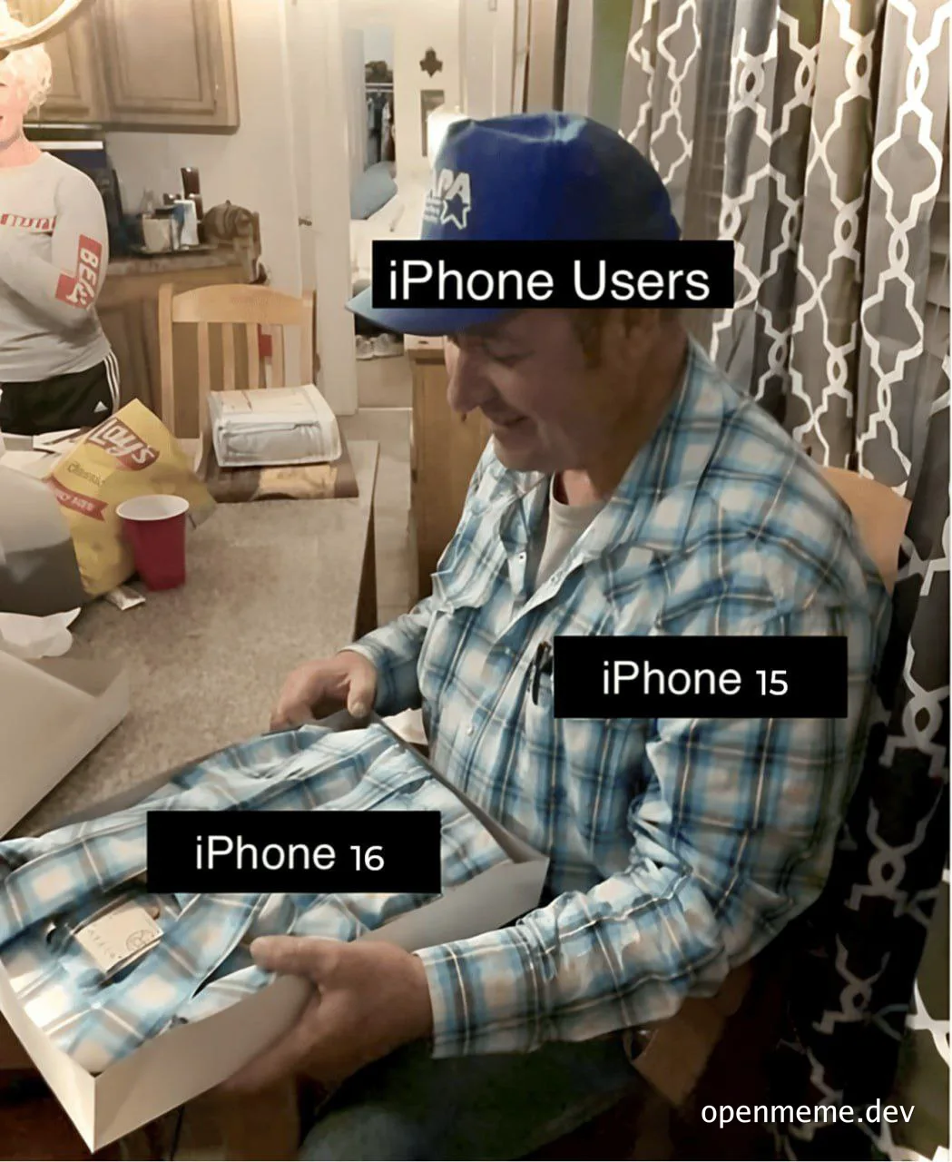 Man in plaid shirt and blue cap opening iPhone 16 box labeled 'iPhone 16', with 'iPhone 15' on his shirt and 'iPhone Users' on his forehead