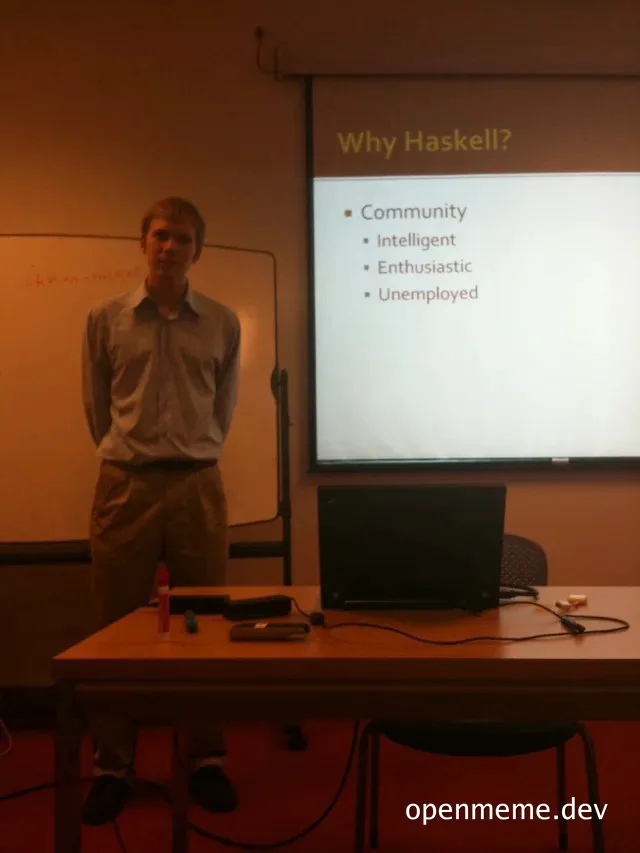 man standing by a table with a laptop and projector screen displaying 'Why Haskell?' with bullet points