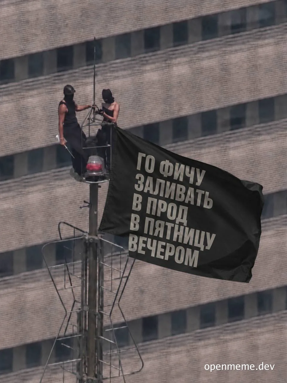 Masked figures hanging a black banner with Russian text 'Going to deploy a feature to production on Friday evening' on a building roof.
