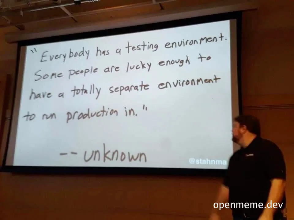 A presenter stands beside a projection screen showing a handwritten quote: "Everybody has a testing environment. Some people