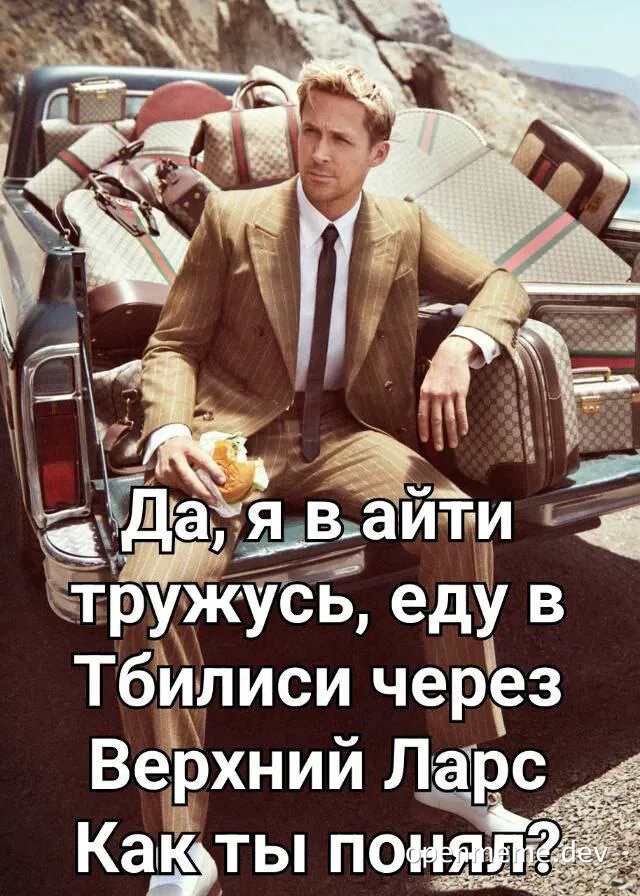 Man in suit sitting in car trunk with luggage, eating sandwich