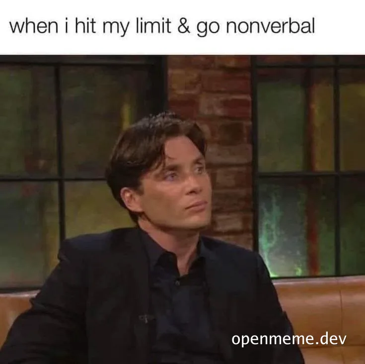 Man in a dark suit sitting on a couch with a deadpan, shut-down expression, captioned 'when i hit my limit & go nonverbal'