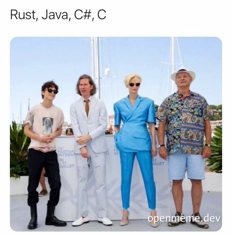 Four people standing in front of a white backdrop with programming languages listed above them