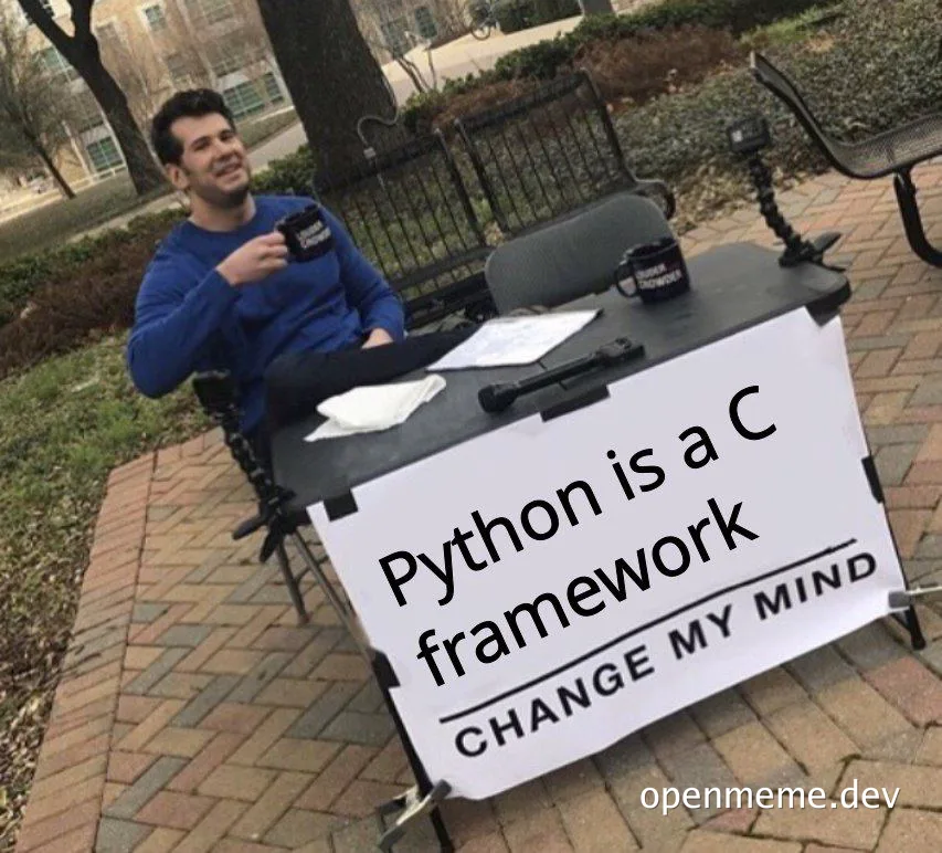 Man sitting at a table with a sign that reads 'Python is a C framework CHANGE MY MIND'