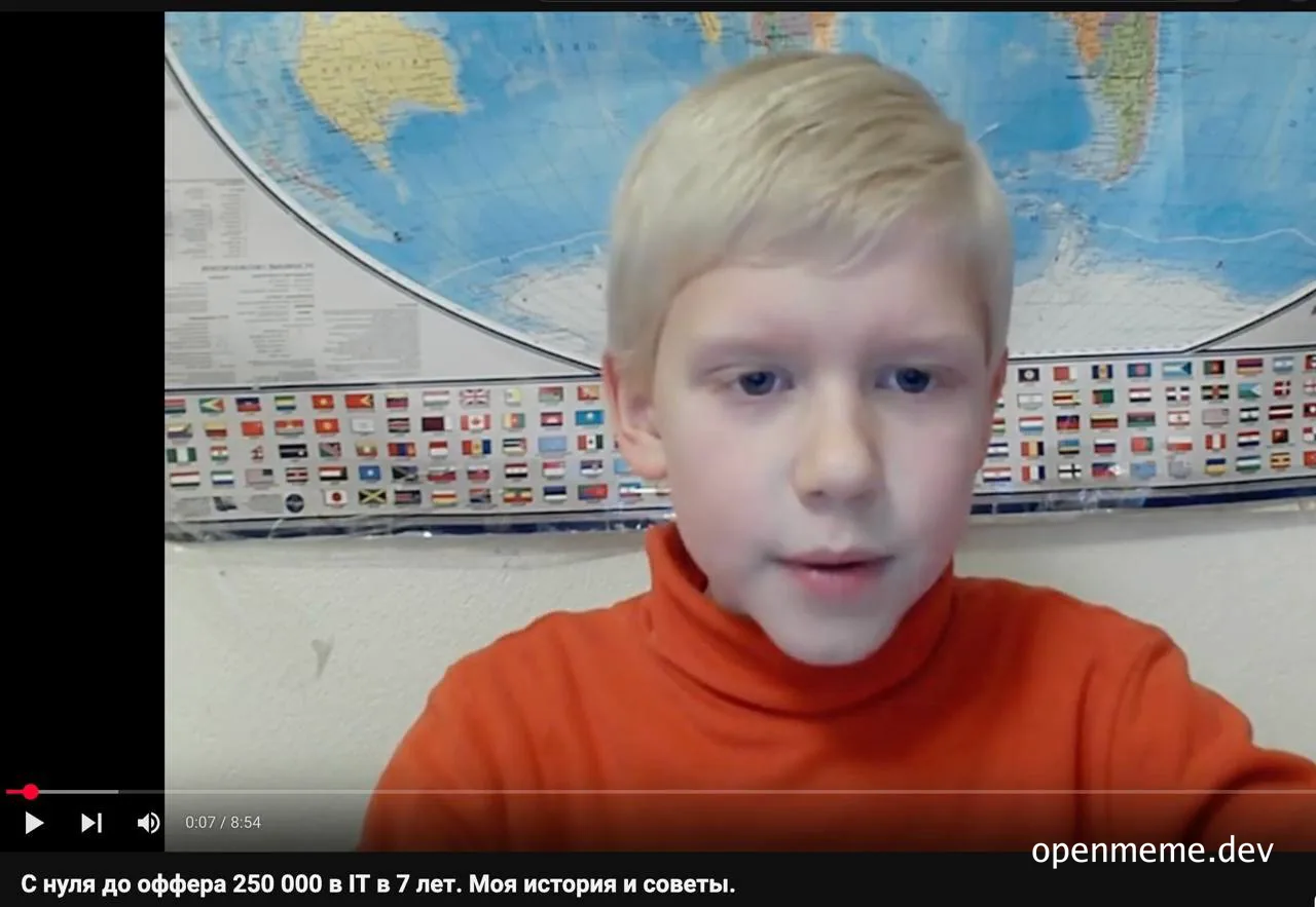 a young boy in an orange turtleneck looks surprised in front of a world map