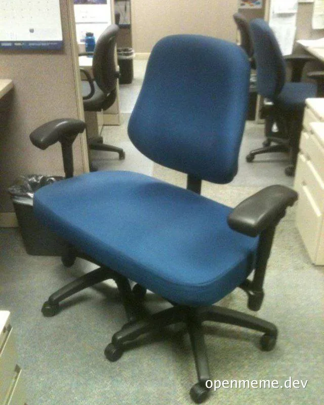 An office chair with a blue seat and backrest, and black armrests and base, positioned in a cubicle.