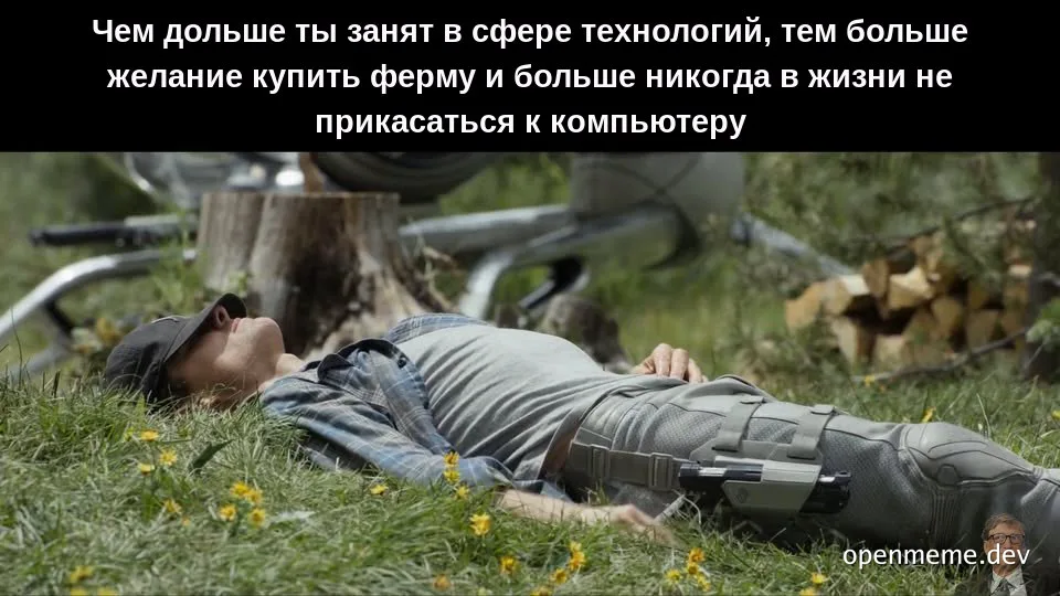 A man in a plaid shirt and cap lies on grass with a VR headset on his legs, a bicycle and woodpile in the background.